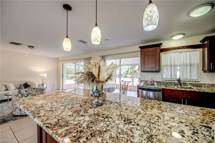 Kitchen with light stone countertops, stainless steel dishwasher, and pendant lighting