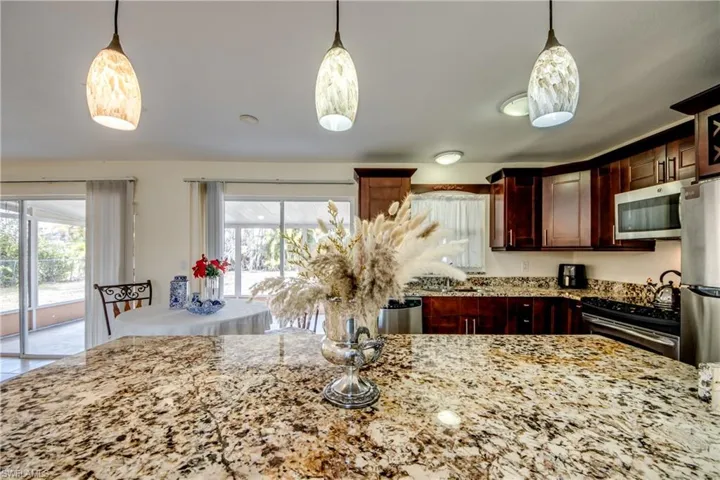 Kitchen with pendant lighting, stainless steel appliances, light stone countertops, and bold wood finish cabinetry