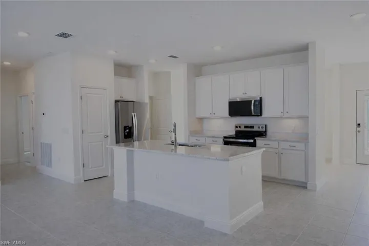 Kitchen featuring stainless steel appliances, white cabinetry, an island with sink, light stone countertops, and recessed lighting