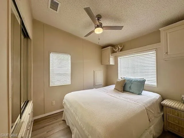 Bedroom with lofted ceiling, light hardwood / wood-style flooring, ceiling fan, and multiple windows