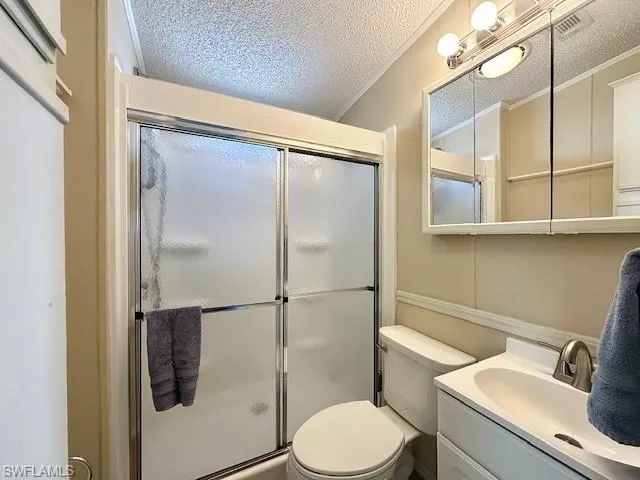 Bathroom featuring a textured ceiling, vanity, an enclosed shower, toilet, and ornamental molding