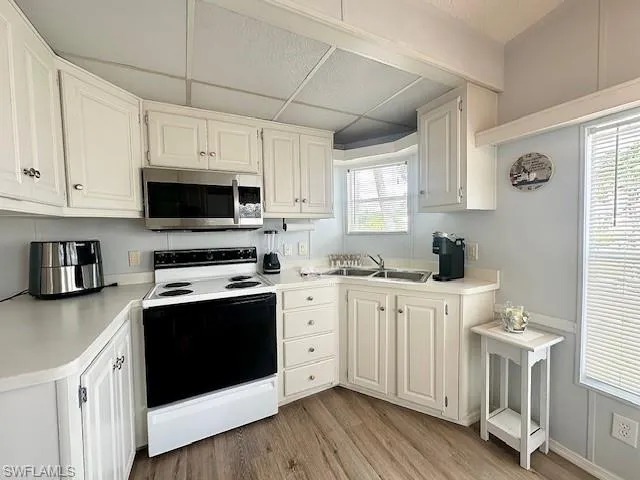 Kitchen with white electric range, sink, white cabinetry, a paneled ceiling, and light wood-type flooring