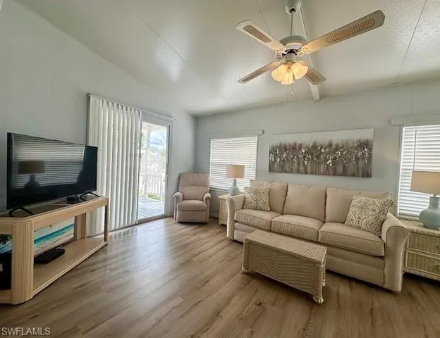 Living room with vaulted ceiling, a textured ceiling, wood-type flooring, and ceiling fan
