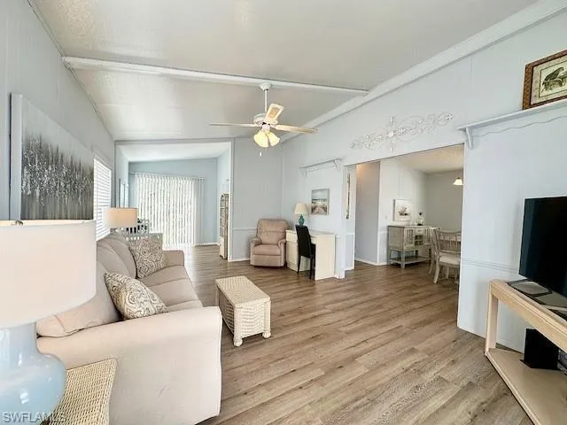 Living room featuring lofted ceiling, light hardwood / wood-style flooring, ceiling fan, and a textured ceiling