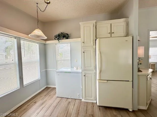 Kitchen featuring light wood-type flooring, white fridge, decorative light fixtures, and a textured ceiling