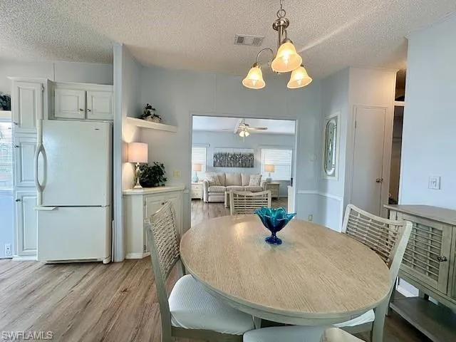 Dining room featuring ceiling fan with notable chandelier, a textured ceiling, and light hardwood / wood-style flooring