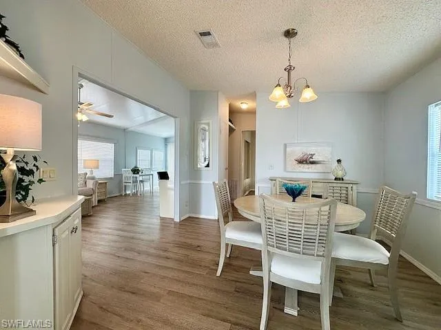 Dining space with ceiling fan with notable chandelier, hardwood / wood-style flooring, and a textured ceiling