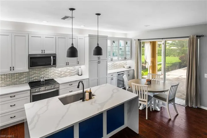 Kitchen with light stone countertops, dark hardwood / wood-style flooring, backsplash, appliances with stainless steel finishes, and sink