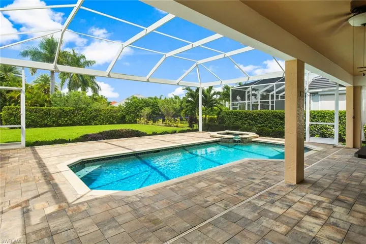 View of pool with glass enclosure, a patio area, and an in ground hot tub