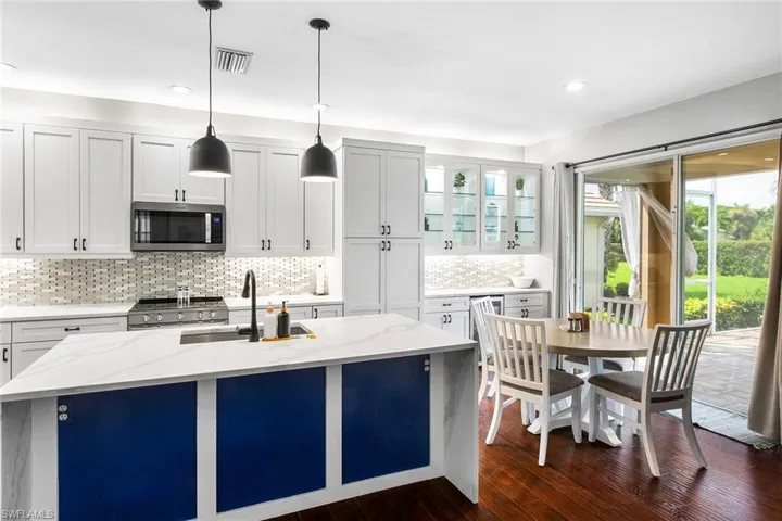Kitchen with appliances with stainless steel finishes, dark hardwood / wood-style flooring, a center island with sink, and light stone countertops