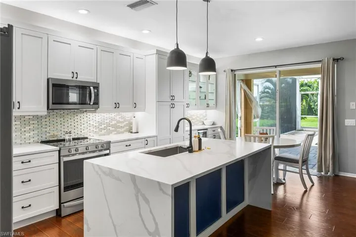 Kitchen with light stone countertops, stainless steel appliances, dark hardwood / wood-style floors, and hanging light fixtures