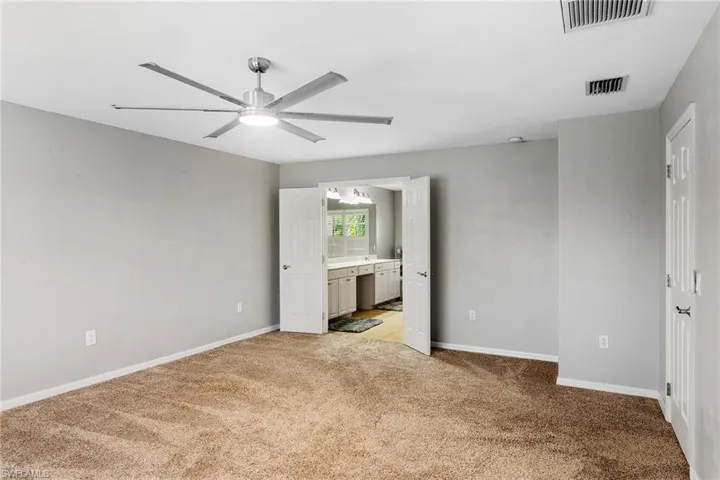 Unfurnished bedroom with ceiling fan, connected bathroom, and light carpet