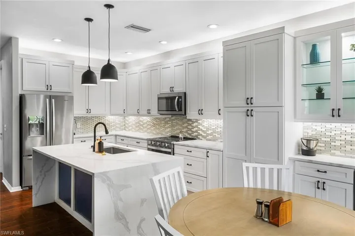 Kitchen featuring backsplash, light stone counters, stainless steel appliances, dark hardwood / wood-style flooring, and pendant lighting