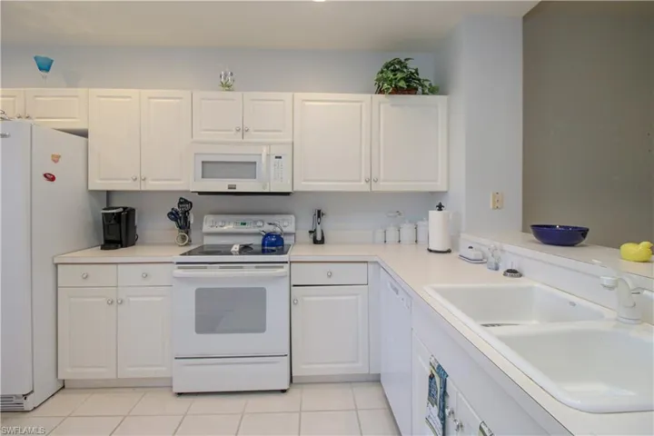 Kitchen with white cabinetry, light tile patterned flooring, white appliances, and sink