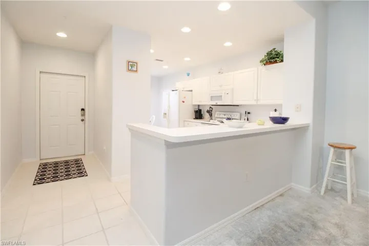 Kitchen featuring white cabinetry, white appliances, kitchen peninsula, and light tile patterned floors
