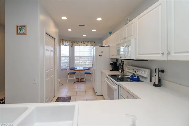 Kitchen with white cabinetry, light tile patterned flooring, white appliances, and sink