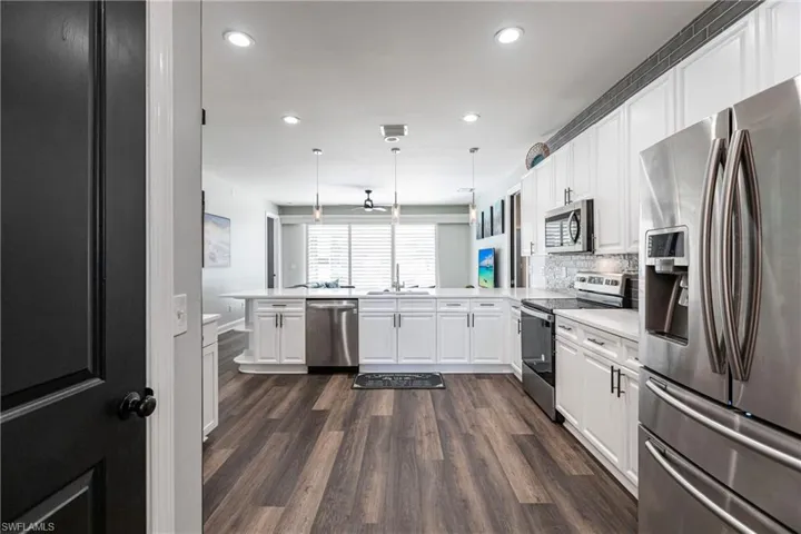 Kitchen featuring white cabinetry, stainless steel appliances, tasteful backsplash, kitchen peninsula, and decorative light fixtures