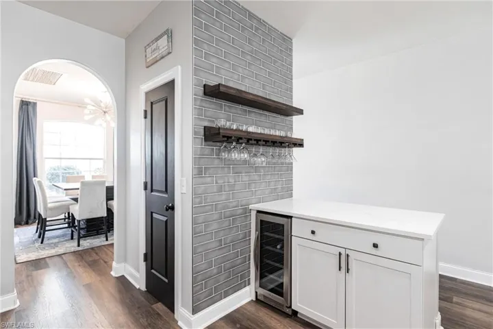 Bar with a chandelier, white cabinetry, beverage cooler, and dark wood-type flooring