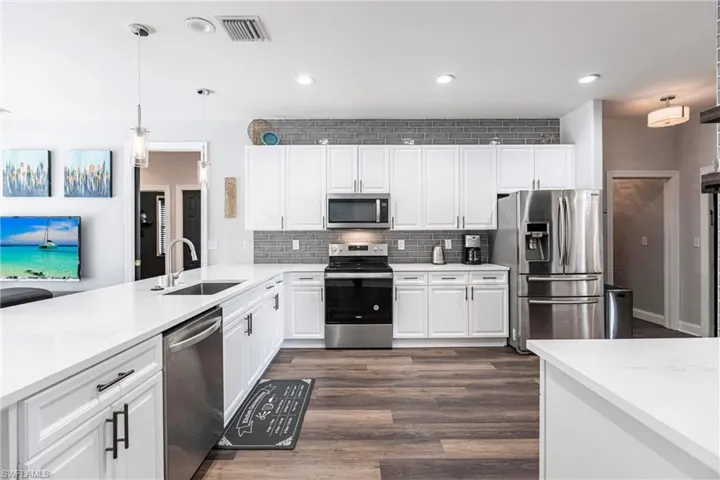 Kitchen featuring light stone countertops, sink, pendant lighting, white cabinets, and appliances with stainless steel finishes