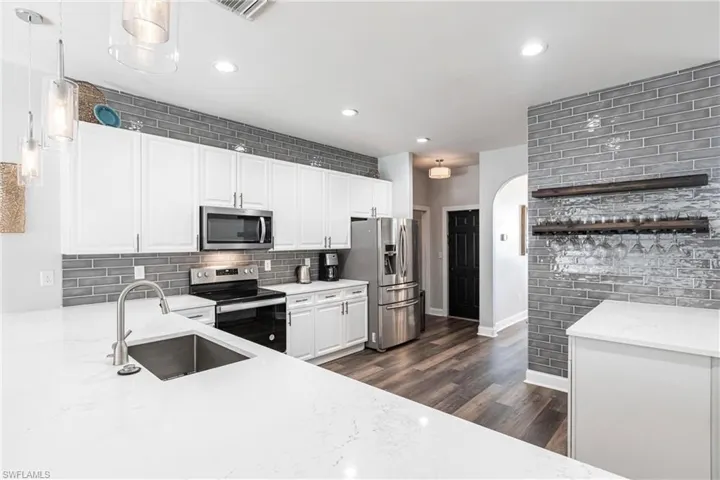 Kitchen with pendant lighting, sink, decorative backsplash, white cabinetry, and stainless steel appliances