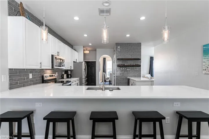 Kitchen featuring sink, kitchen peninsula, pendant lighting, white cabinets, and appliances with stainless steel finishes