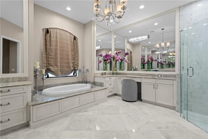 Spacious bathroom featuring a built-in soaking tub, framed vanity mirrors, a glass-enclosed shower, white cabinetry, and light-toned tile flooring