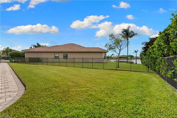 Expansive backyard with a manicured lawn, paver patio border, and black metal fencing