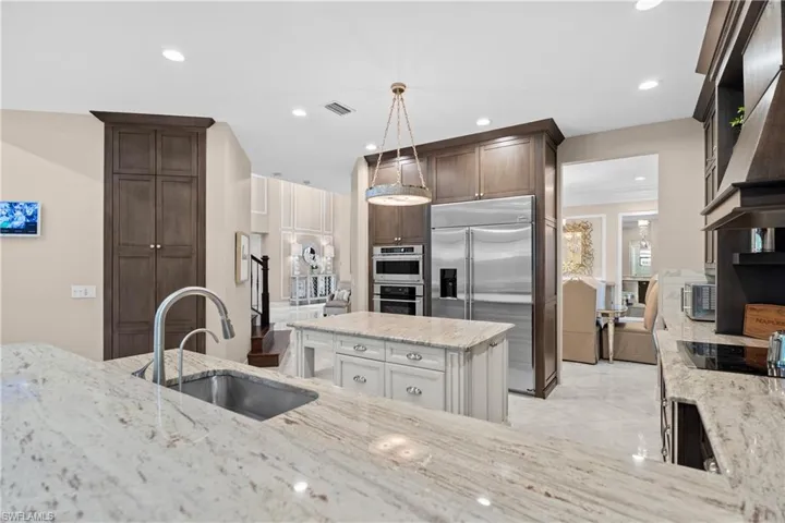Gourmet kitchen featuring granite countertops, stainless steel appliances, dark wood cabinetry, a central island with additional storage, and recessed lighting