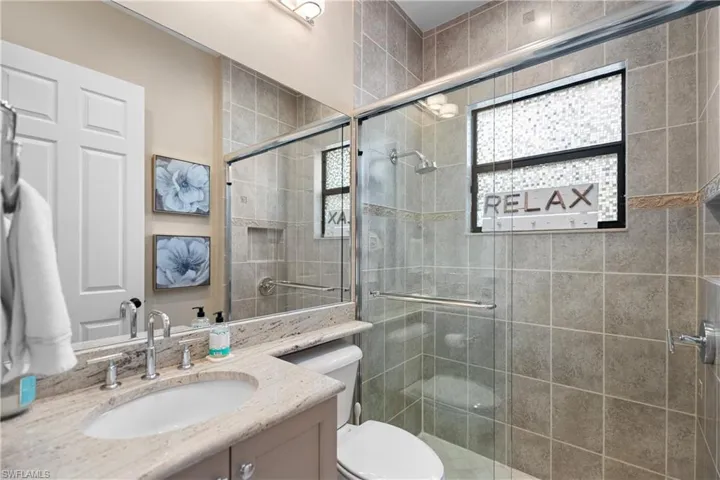 Bathroom featuring a glass-enclosed shower with tile surround, a built-in shower niche, and a window with privacy film