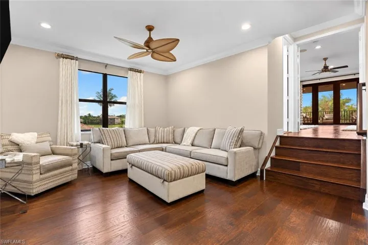 Spacious living area featuring rich wood-finish flooring, a large window with exterior views, and crown molding