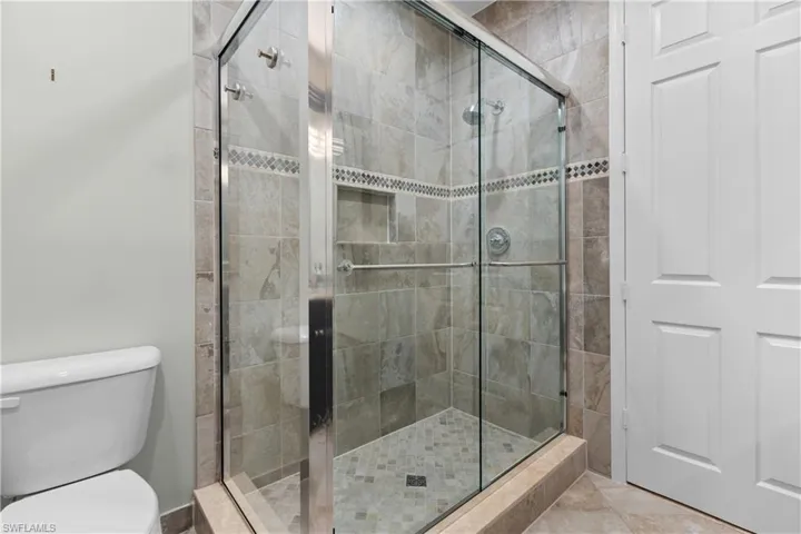 Glass-enclosed shower featuring a tiled surround with decorative accent band, built-in shelving, and a mosaic-tiled floor