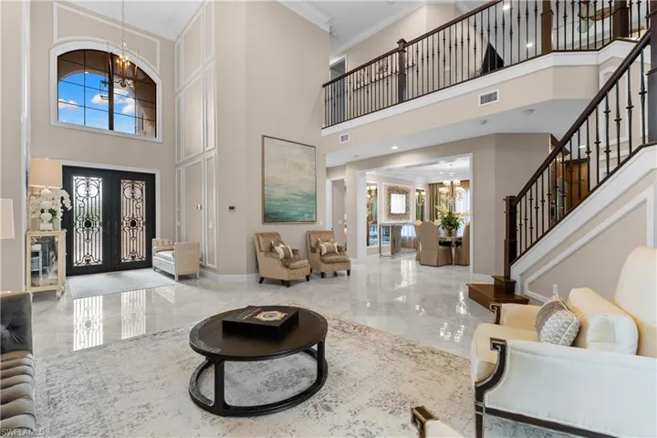 Grand foyer featuring a double-height ceiling, arched transom window, and dual entry doors with decorative ironwork