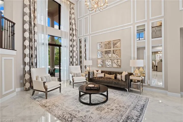 Two-story living area featuring tall windows and a glass door, intricate wall molding, a balcony with iron railings, and polished tile flooring