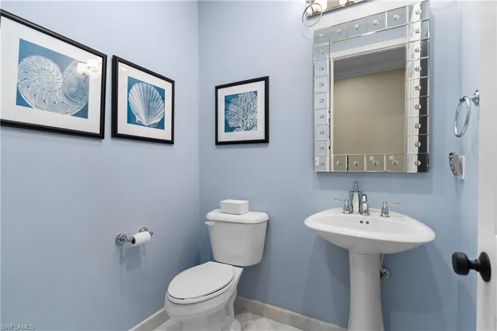 Pedestal sink with chrome fixtures, framed decorative mirror, and light blue wall finish