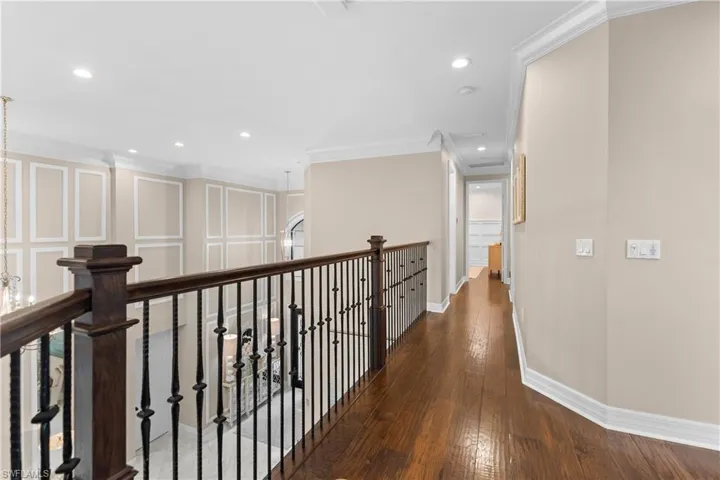 Upper-level hallway featuring rich wood-finish flooring, a wrought iron and wood balustrade, recessed lighting, crown molding, and wainscoting details