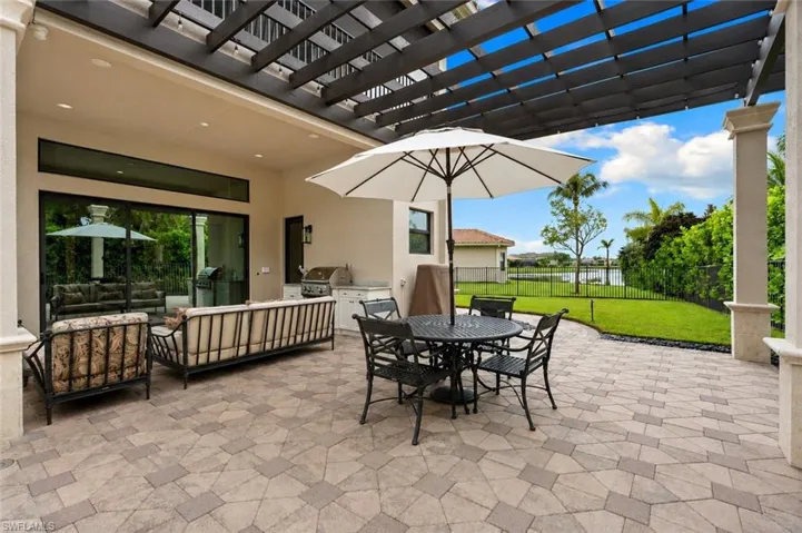 Expansive outdoor living area featuring a patterned paver patio, a custom pergola, and a built-in outdoor kitchen with a grill
