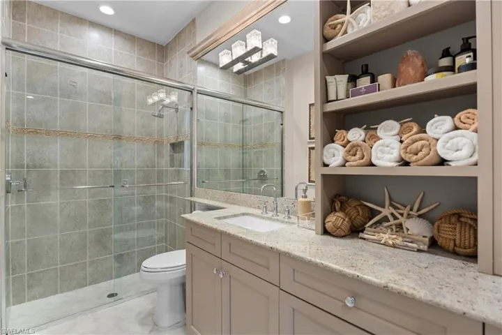 Bathroom featuring a glass-enclosed shower with tile surround, a built-in shower niche, a single vanity with stone countertop, and an integrated open shelving unit