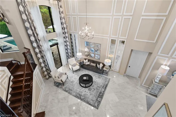 Grand two-story living area featuring tall windows with exterior pool views, a classic chandelier, paneled wall accents, and light-toned tile flooring