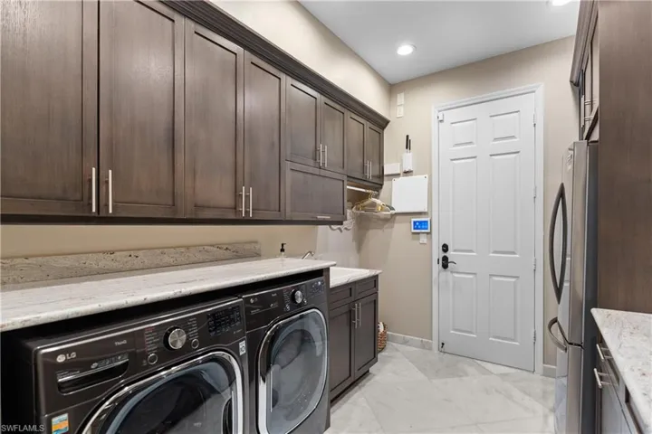 Laundry area featuring extensive dark wood-finish cabinetry, light-toned stone countertops, built-in appliances, and light tile flooring