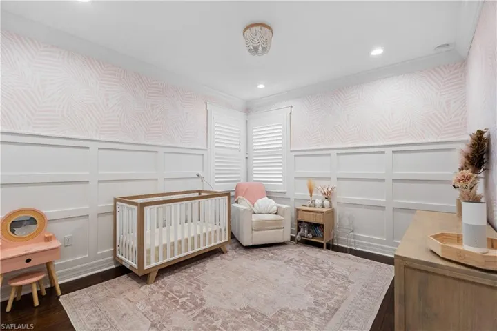 Room featuring dark wood-finish flooring, white wainscoting, and patterned wallpaper