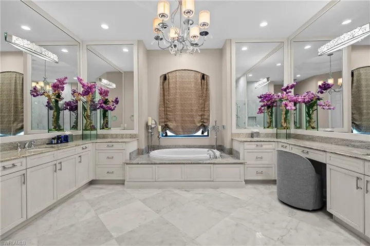 Expansive bathroom featuring a built-in soaking tub, dual vanity areas with stone countertops, and extensive white cabinetry