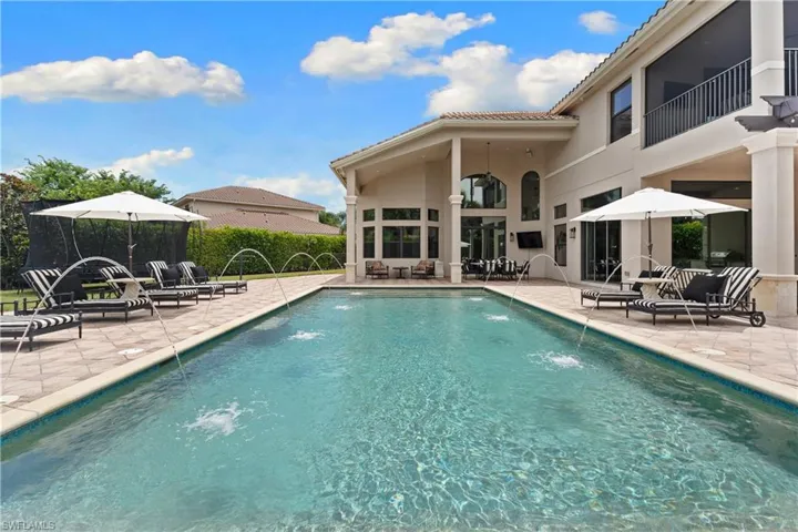 Expansive outdoor living area featuring a rectangular swimming pool with fountain jets, surrounded by a paver patio