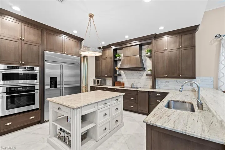 Expansive kitchen featuring a double oven, stainless steel refrigerator, and a large island with an integrated sink