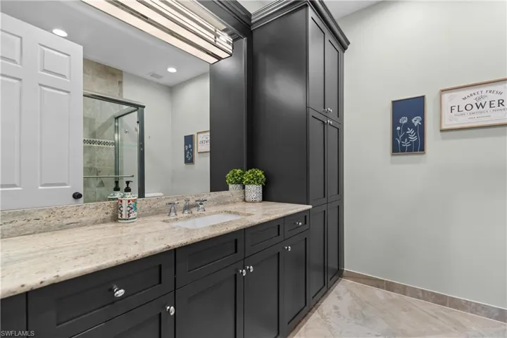 Bathroom vanity featuring a light-toned stone countertop, dark cabinetry, and integrated sink