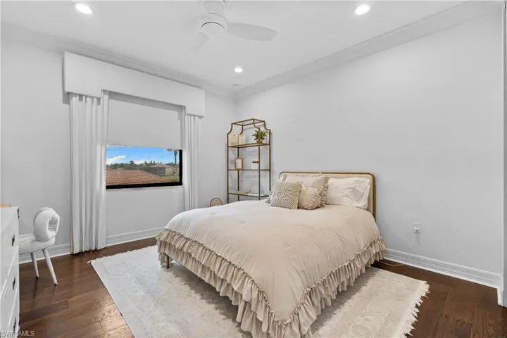 Bedroom featuring rich wood-finish flooring, white walls, and crown molding