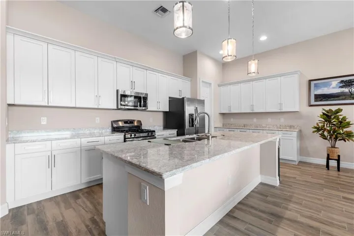 center island with sink, appliances with stainless steel finishes, and hanging light fixtures