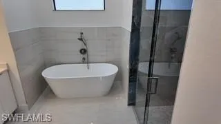 Full bath featuring vanity, a marble finish shower, tile walls, and a soaking tub
