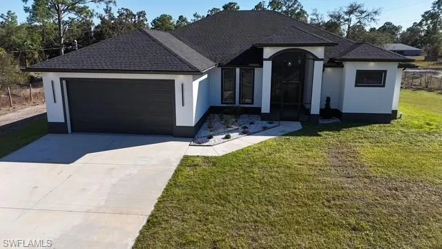 View of front of home with stucco siding, a garage, driveway, a front lawn, and roof with shingles