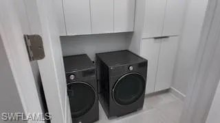 Laundry room with cabinet space, washer and clothes dryer, and light tile patterned flooring