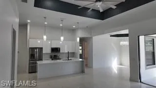 Kitchen with light countertops, a high tray ceiling, white cabinetry, stainless steel appliances, and decorative light fixtures